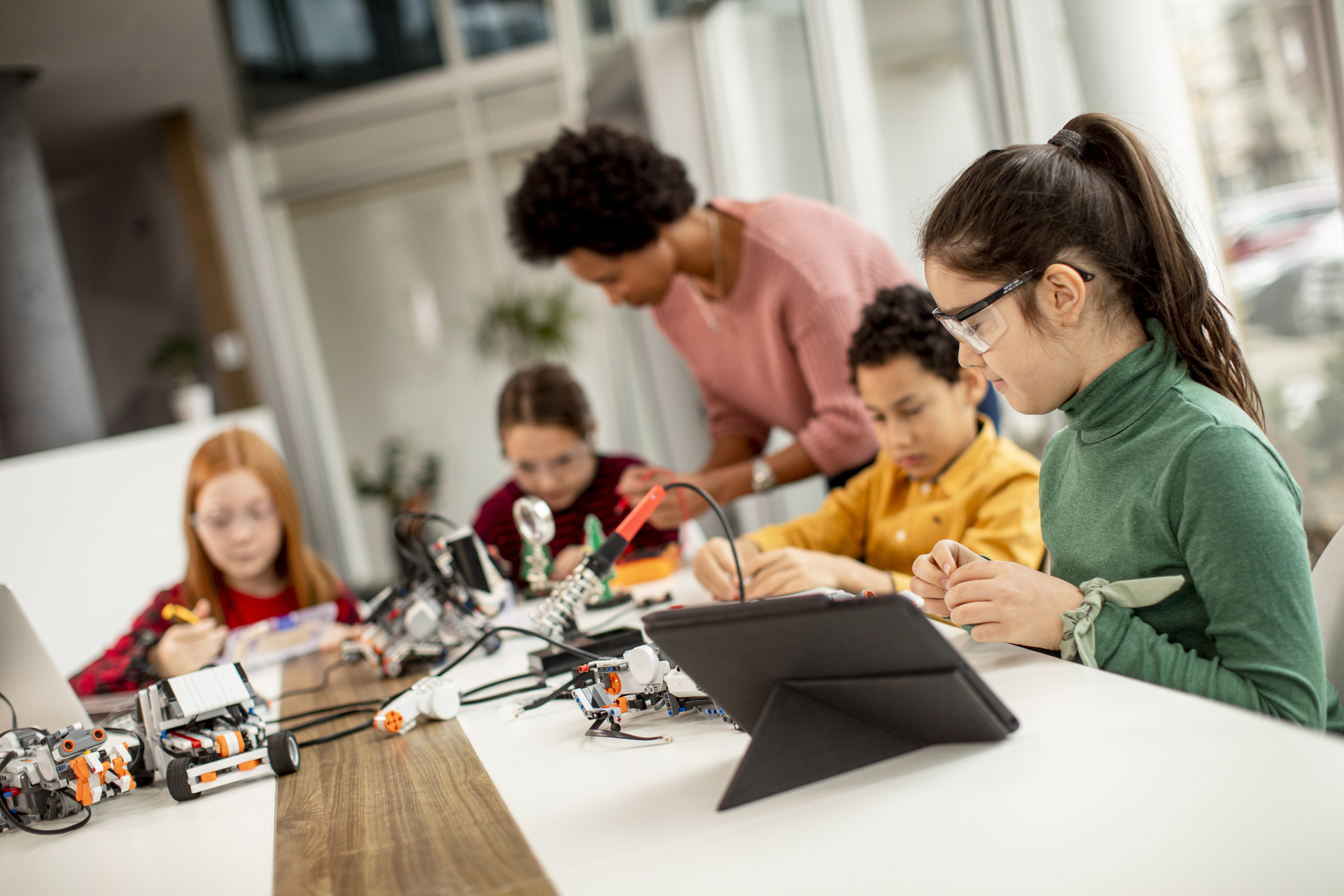 Teacher supporting pupils during a hands-on STEM activity using robotics and tablets in a classroom