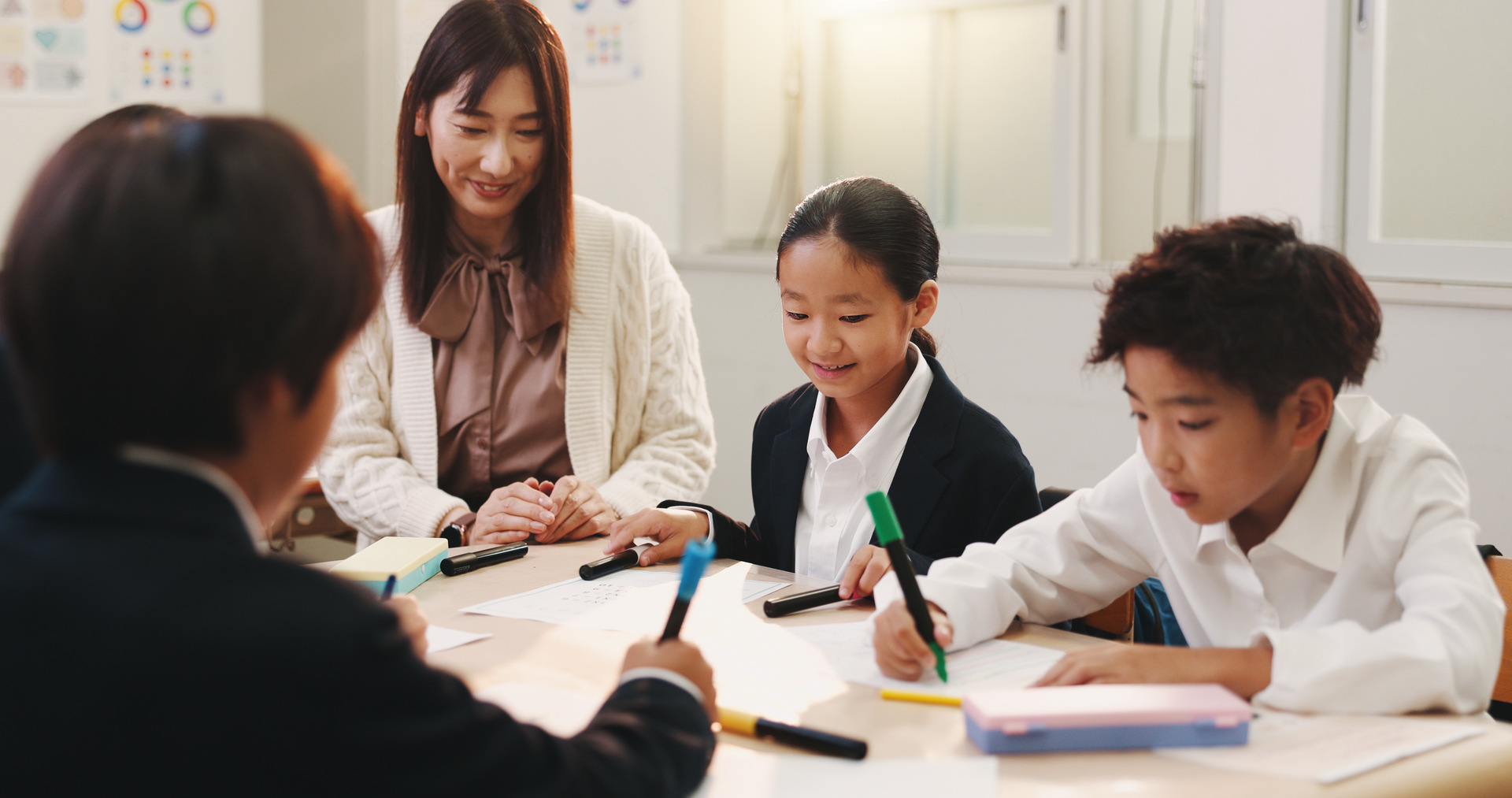 teacher supporting students with work at classroom table