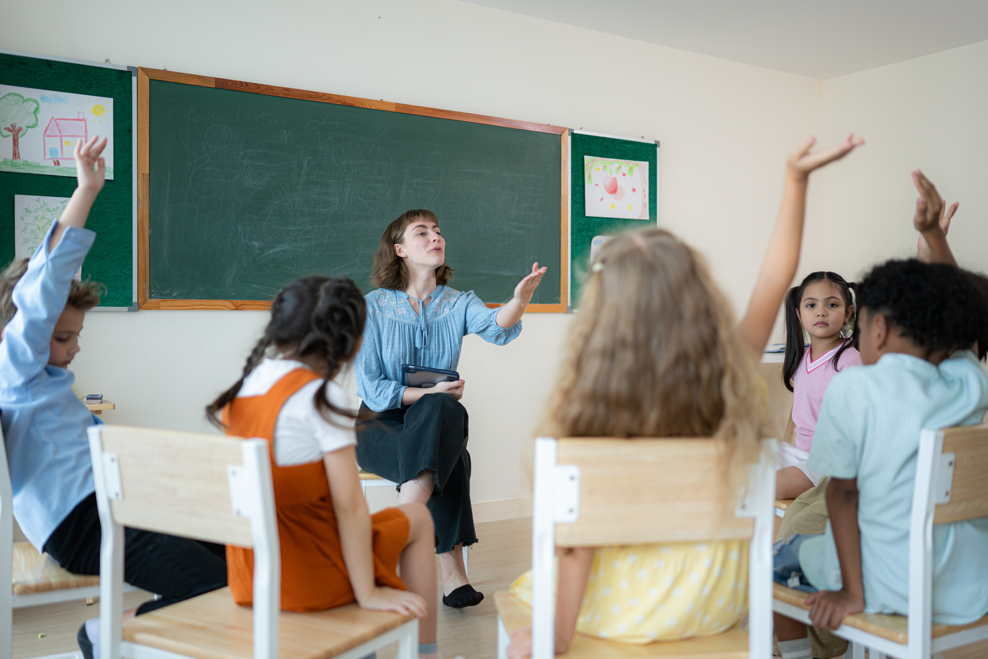 Teacher leading a classroom discussion while pupils raise their hands to participate