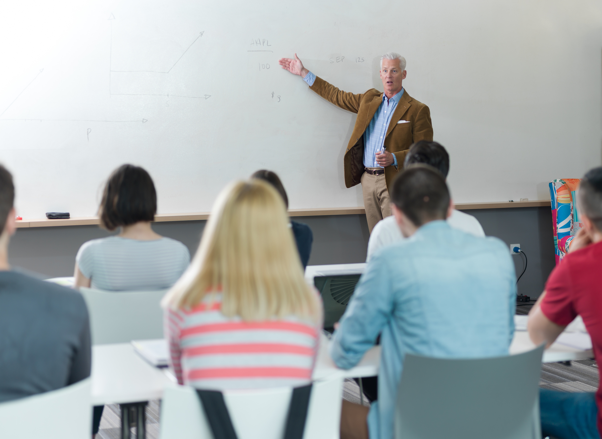 Teacher pointing at a whiteboard while delivering a lesson to students seated in a classroom
